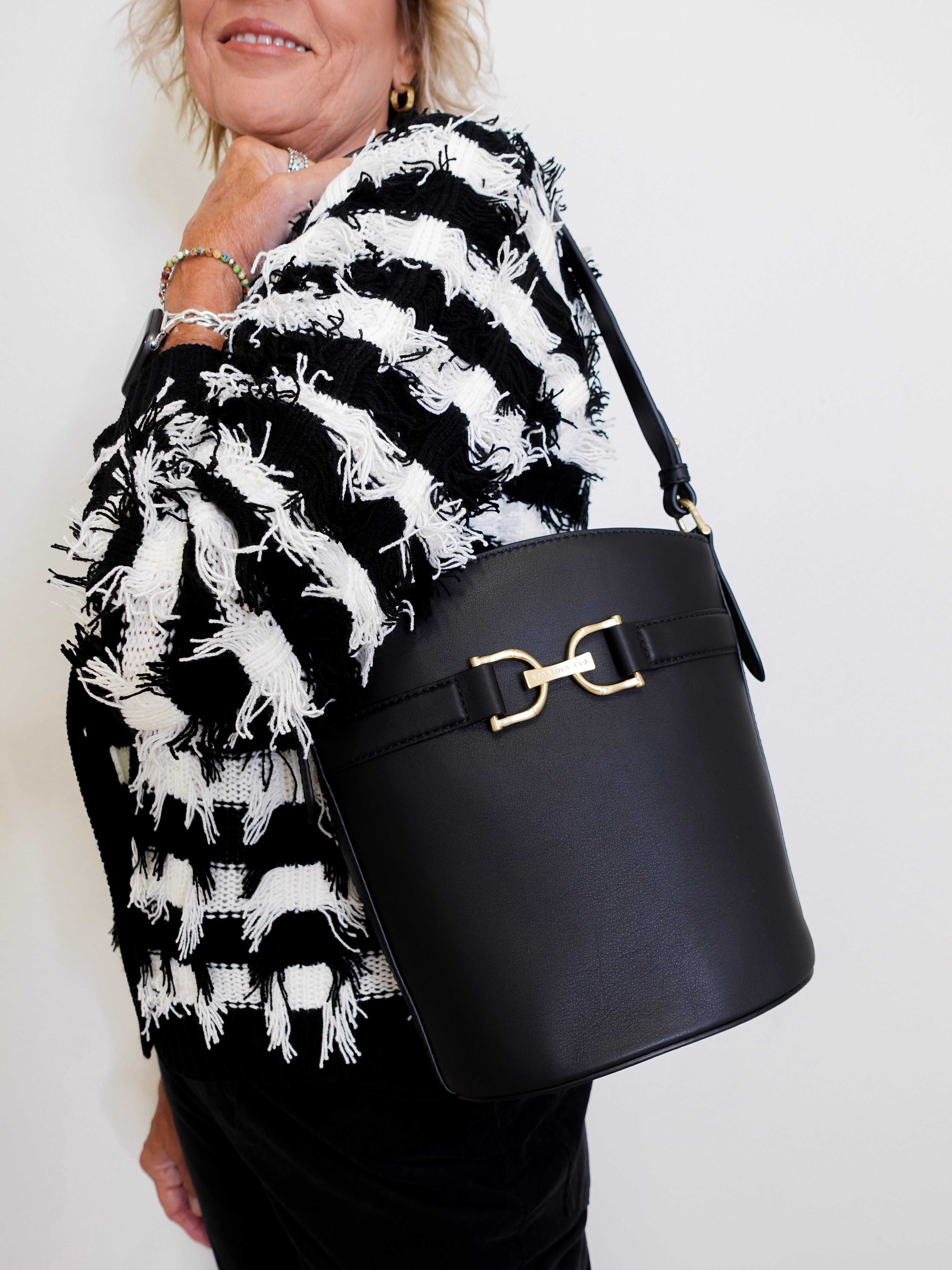 Person wearing a black and white patterned coat holding a black handbag with a gold clasp.