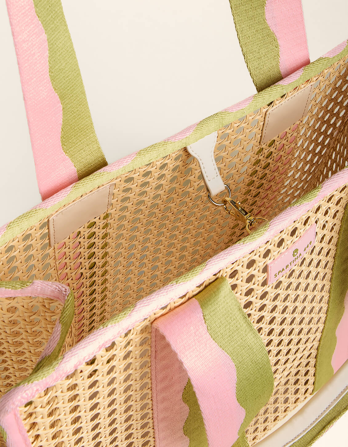Close-up of a woven bag with pink and green striped handles on a light background