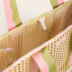 Close-up of a woven bag with pink and green striped handles on a light background
