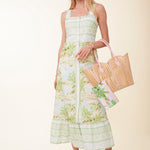 Woman wearing a floral dress holding a woven bag on a beige background