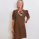 Woman wearing a brown dress with ruffled sleeves against a white wall