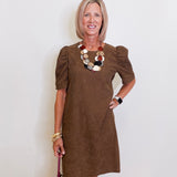 Woman wearing a brown dress with ruffled sleeves against a white wall