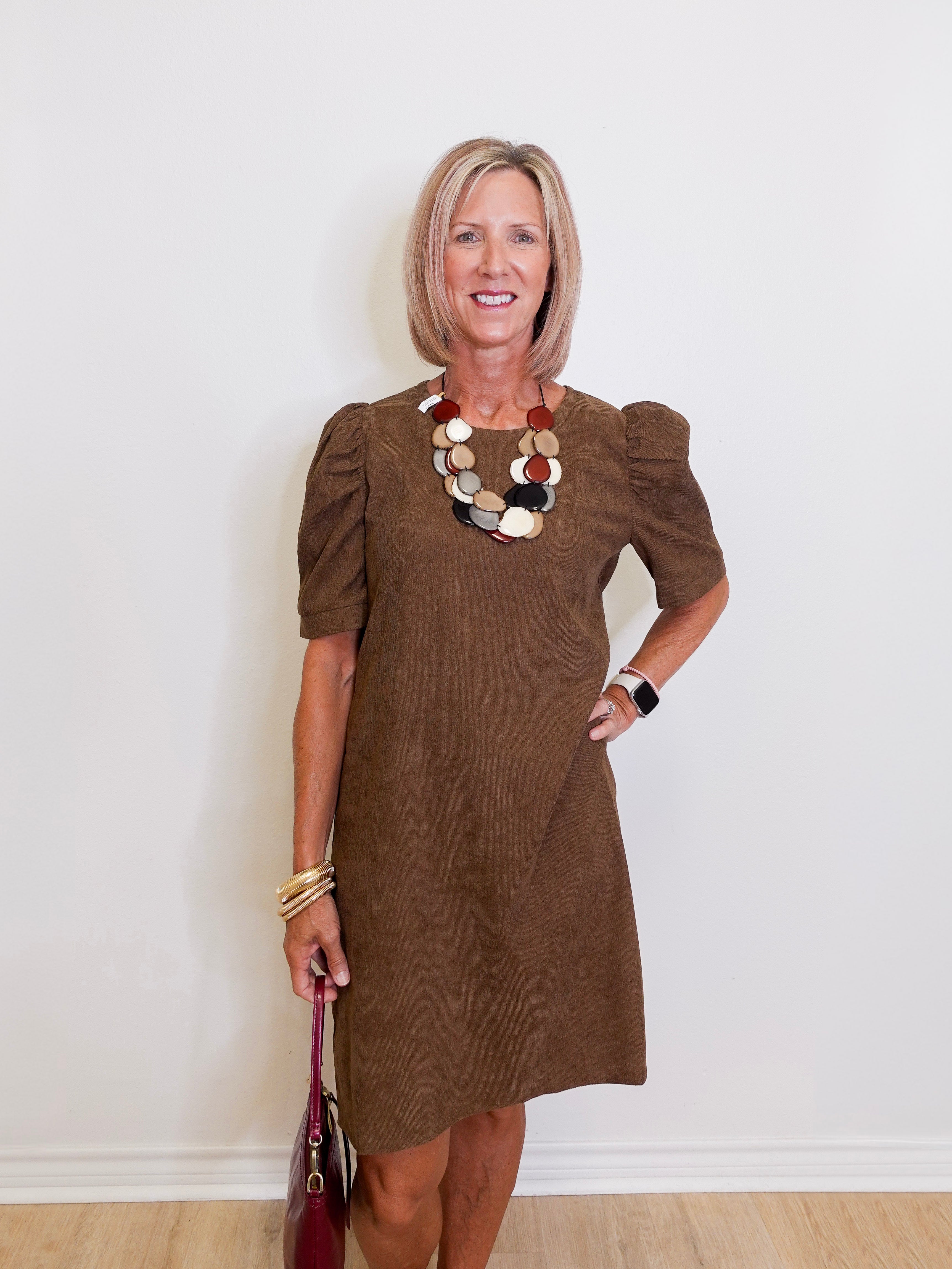 Woman wearing a brown dress with ruffled sleeves against a white wall