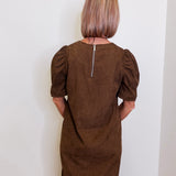 Woman wearing a brown dress with puff sleeves against a white wall