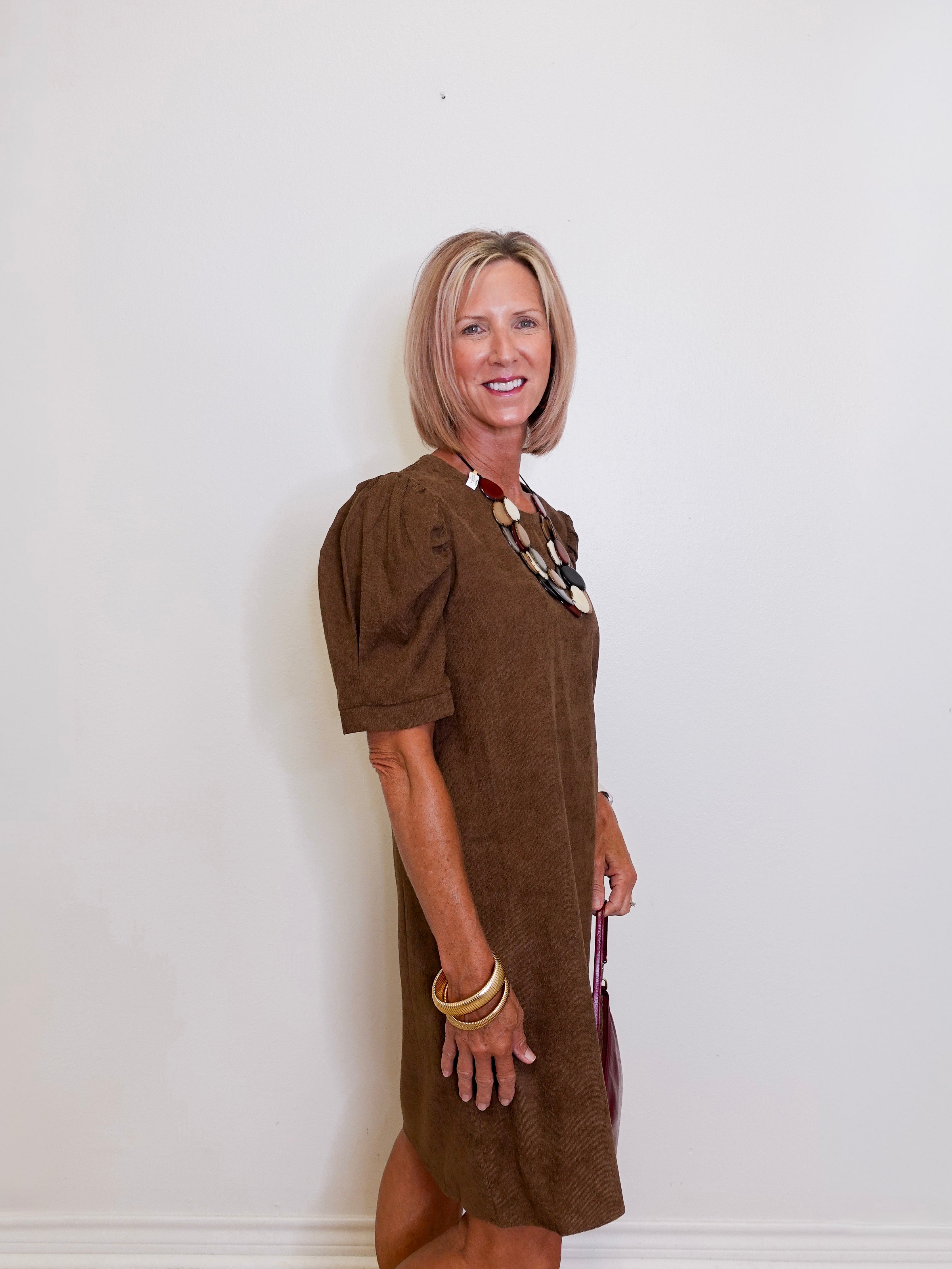 Woman wearing a brown dress against a white wall