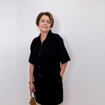 Woman wearing a black dress holding a brown handbag against a white wall.