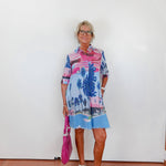 Woman wearing a colorful dress with palm tree design against a white wall.