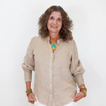 Woman wearing a beige shirt and white pants against a white background