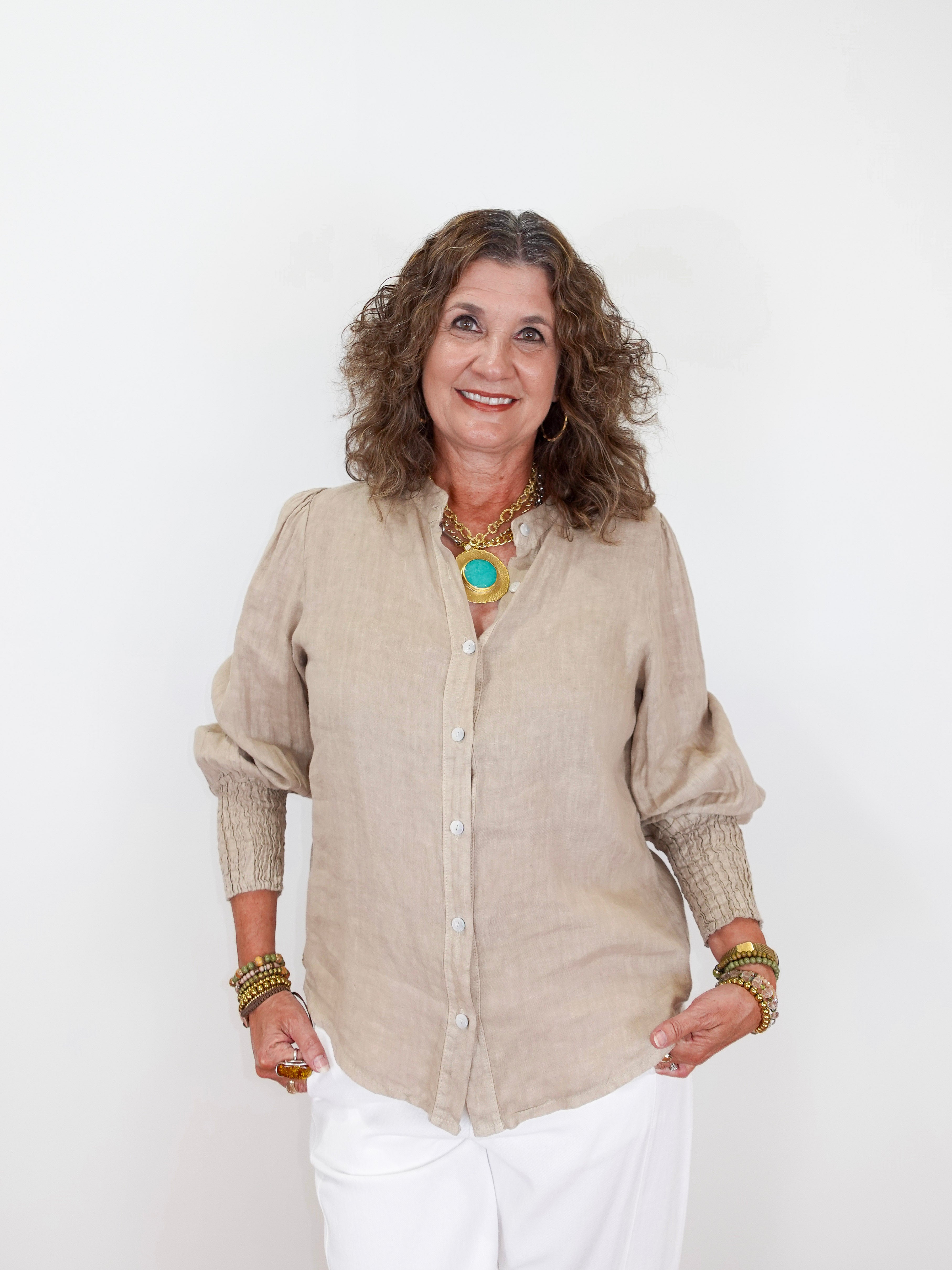 Woman wearing a beige shirt and white pants against a white background