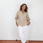 Woman wearing a beige shirt and white pants against a plain white background