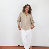 Woman wearing a beige shirt and white pants against a plain white background