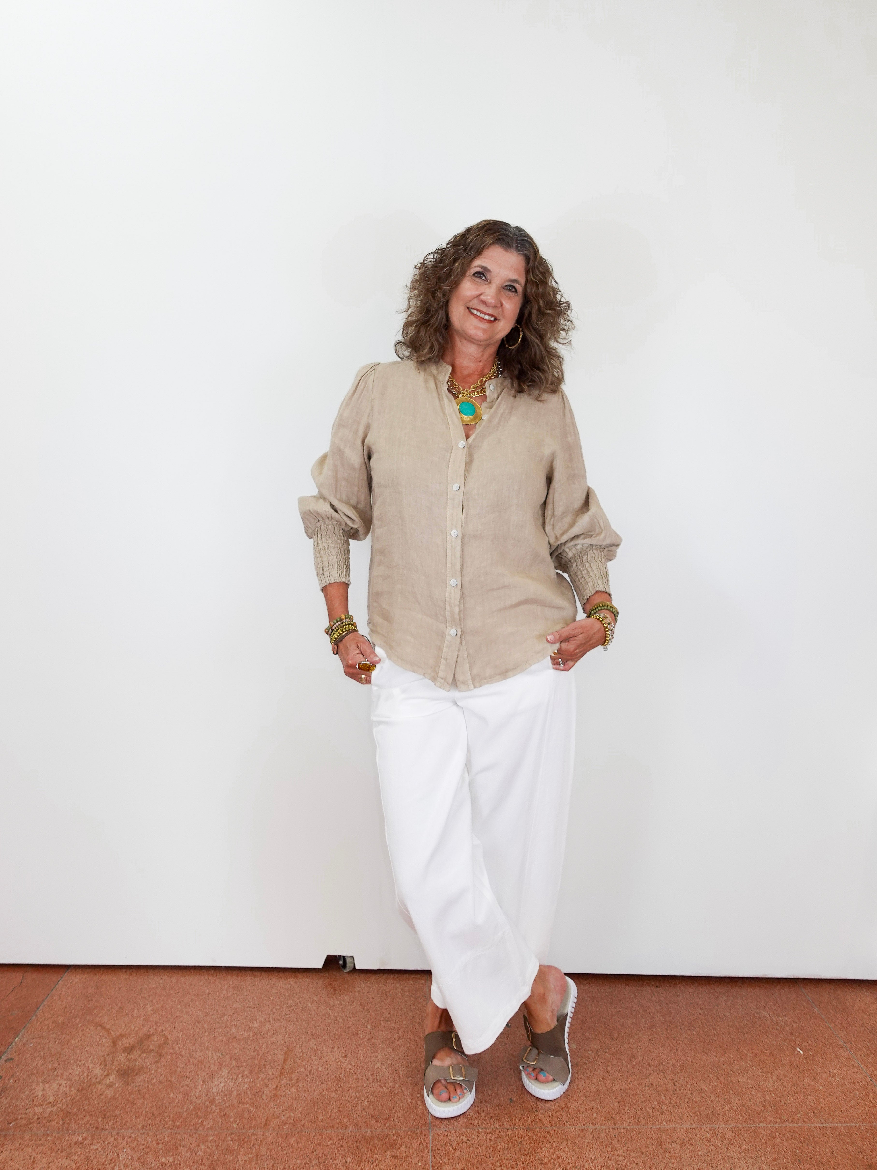 Woman wearing a beige shirt and white pants against a plain white background