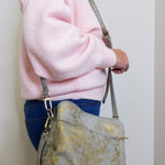 Person wearing a pink sweater and holding a gold handbag against a plain background