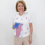 Woman wearing a white blouse with red and blue patterns, holding a matching bag against a white background