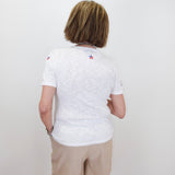 Person wearing a white t-shirt with small logos on the back, standing against a plain white wall.