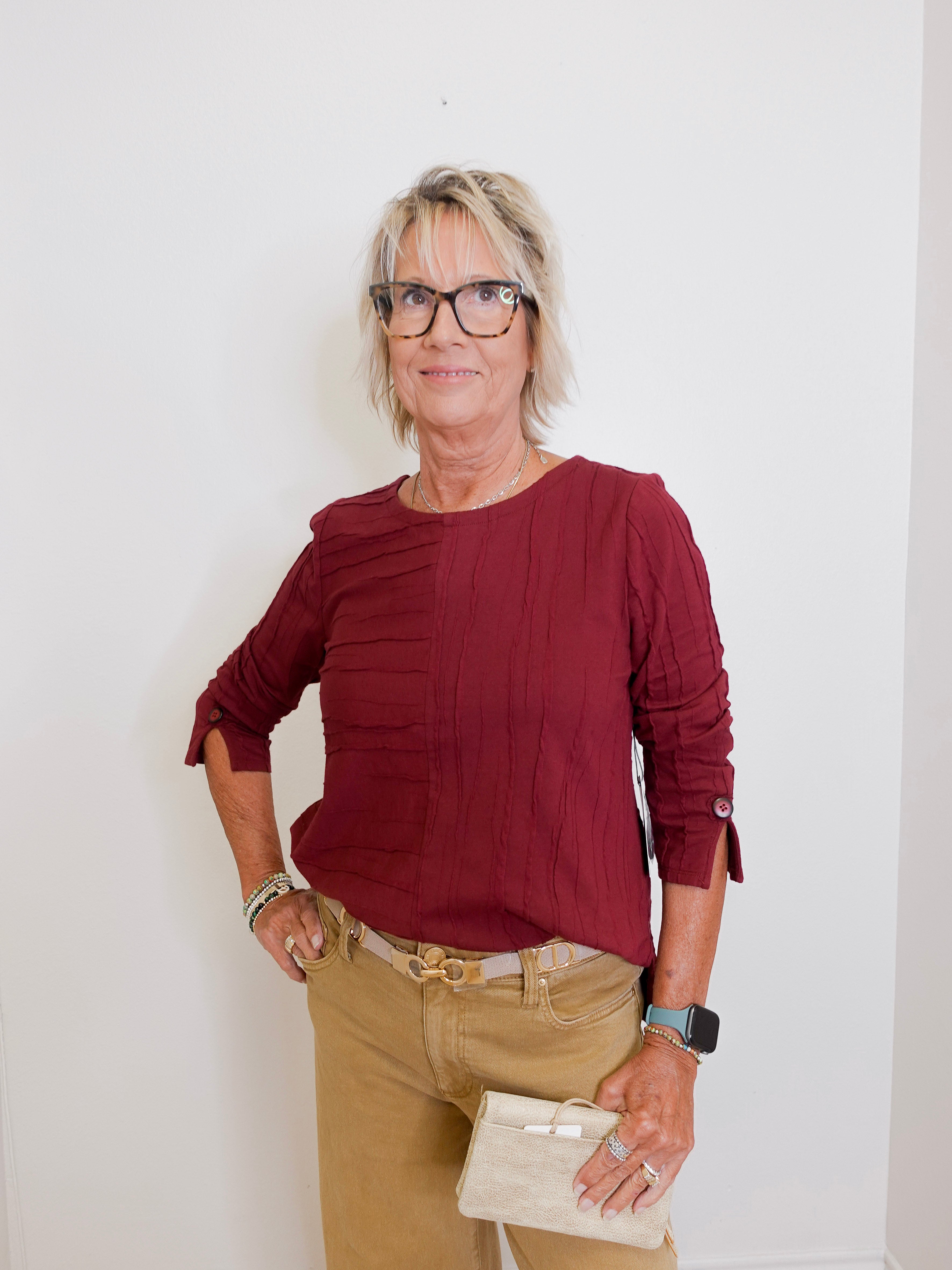 Woman wearing a burgundy top and beige pants against a white background