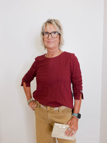 Woman wearing a burgundy top and beige pants against a white background