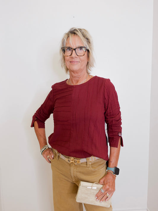 Woman wearing a burgundy top and beige pants against a white background