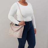 Person wearing a white long-sleeve top and dark blue jeans, holding a beige handbag against a plain background