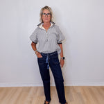 Person wearing a striped shirt and dark jeans standing against a white wall.