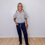 Person wearing a striped shirt and dark jeans standing against a white wall.