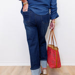 Person wearing blue jeans and a blue top, holding a red patterned bag on a light wooden floor.