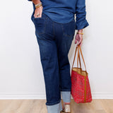 Person wearing blue jeans and a blue top, holding a red patterned bag on a light wooden floor.