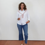 Woman wearing a white blouse with a patterned scarf, blue jeans, and sandals against a white wall.