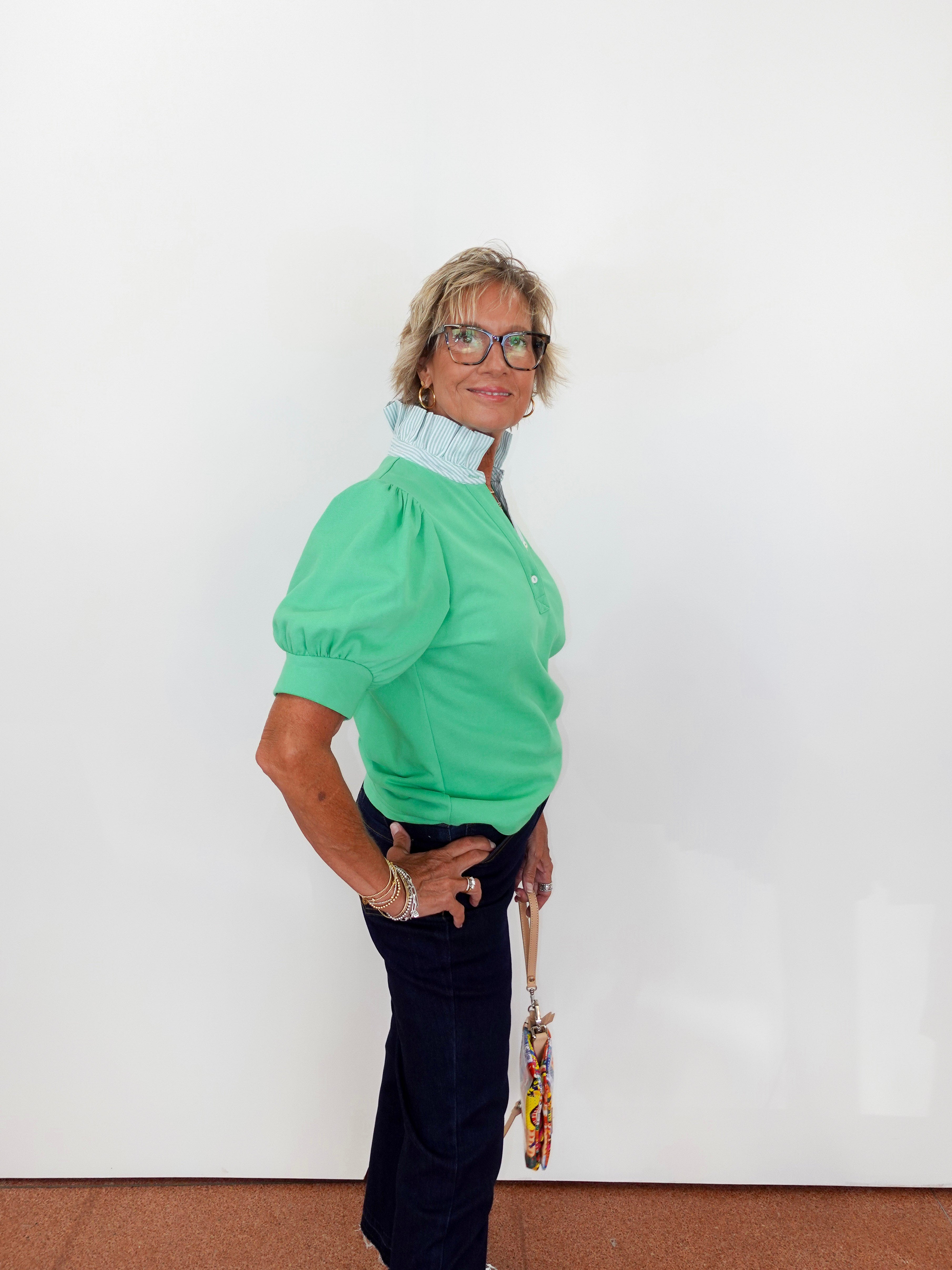Woman wearing a green blouse with puffed sleeves against a white wall.