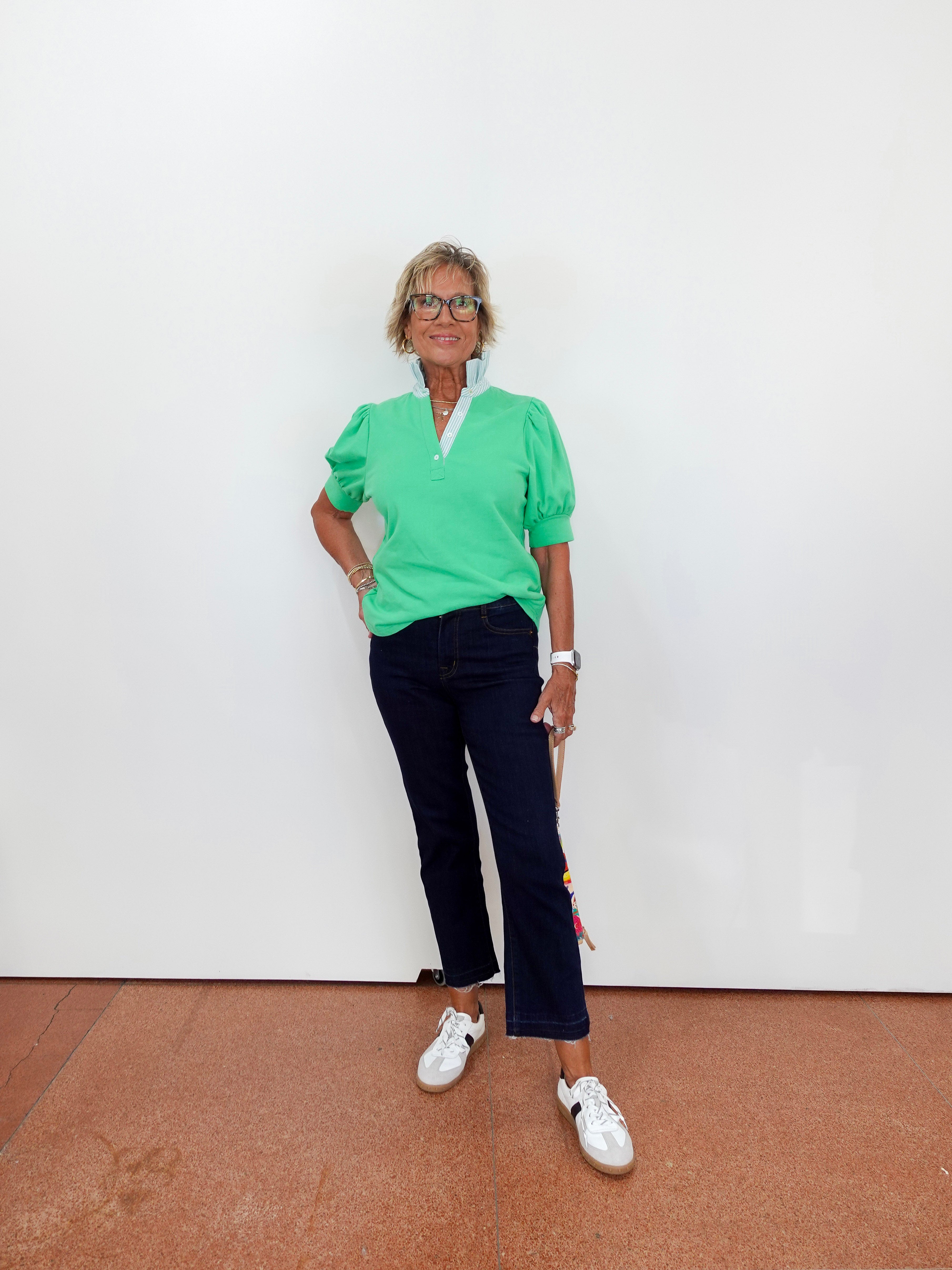 Person wearing a green top and dark pants standing against a white wall.