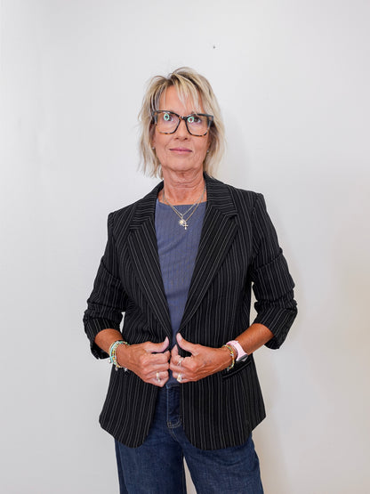 Person wearing a black pinstripe blazer over a blue shirt with a plain background