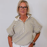 Woman wearing a striped shirt and white pants against a plain background