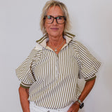 Woman wearing a striped shirt and white pants against a plain background