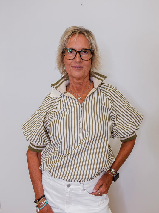 Woman wearing a striped shirt and white pants against a plain background