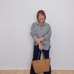 Woman holding a beige handbag against a white wall