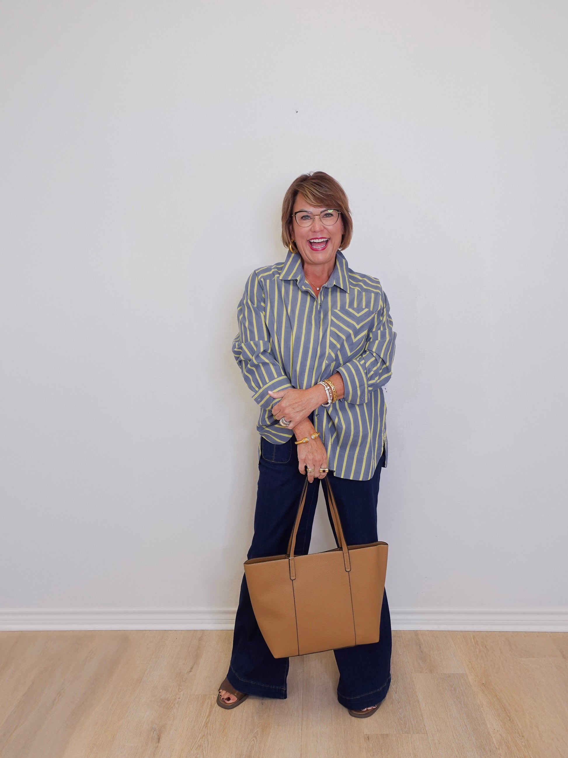Woman holding a beige handbag against a white wall