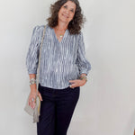 Woman wearing a striped shirt and navy pants against a white wall