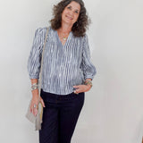 Woman wearing a striped shirt and navy pants against a white wall