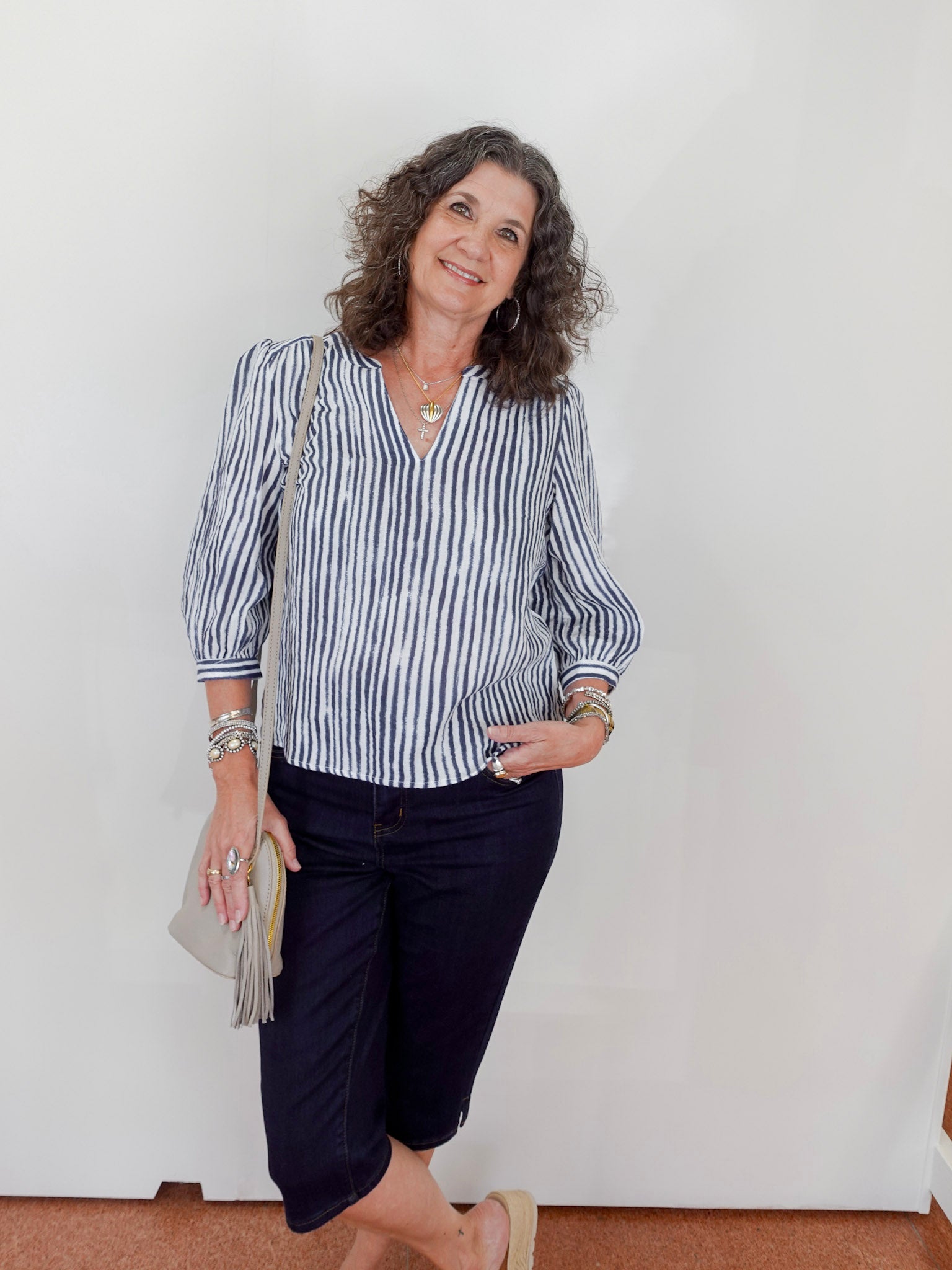 Woman wearing a striped shirt and navy pants against a white wall