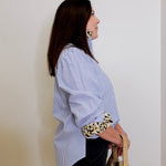 Woman wearing a blue and white striped shirt with a leopard print belt against a plain background