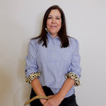 Woman wearing a blue striped shirt with leopard print cuffs against a plain background