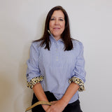 Woman wearing a blue striped shirt with leopard print cuffs against a plain background