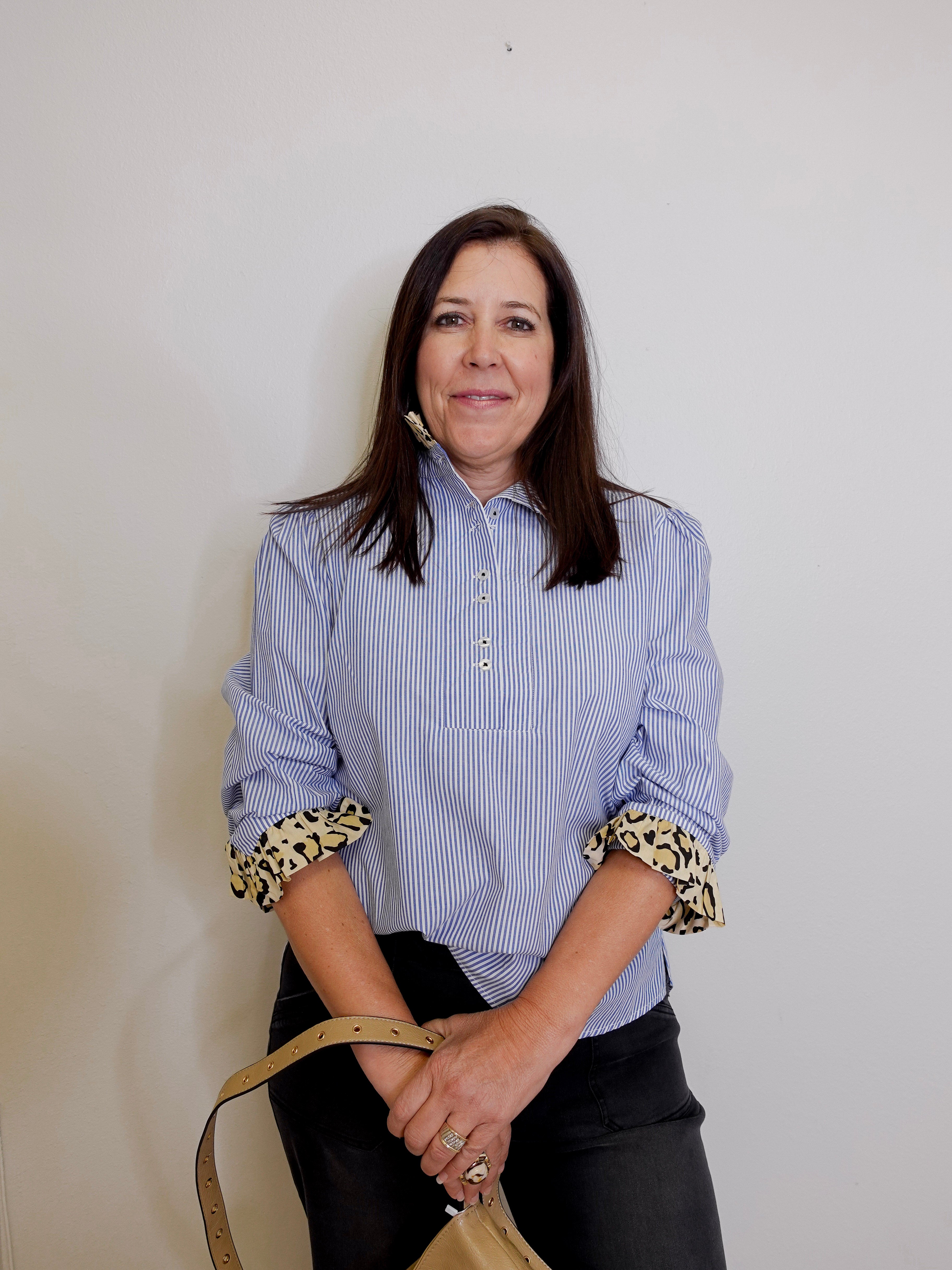 Woman wearing a blue striped shirt with leopard print cuffs against a plain background
