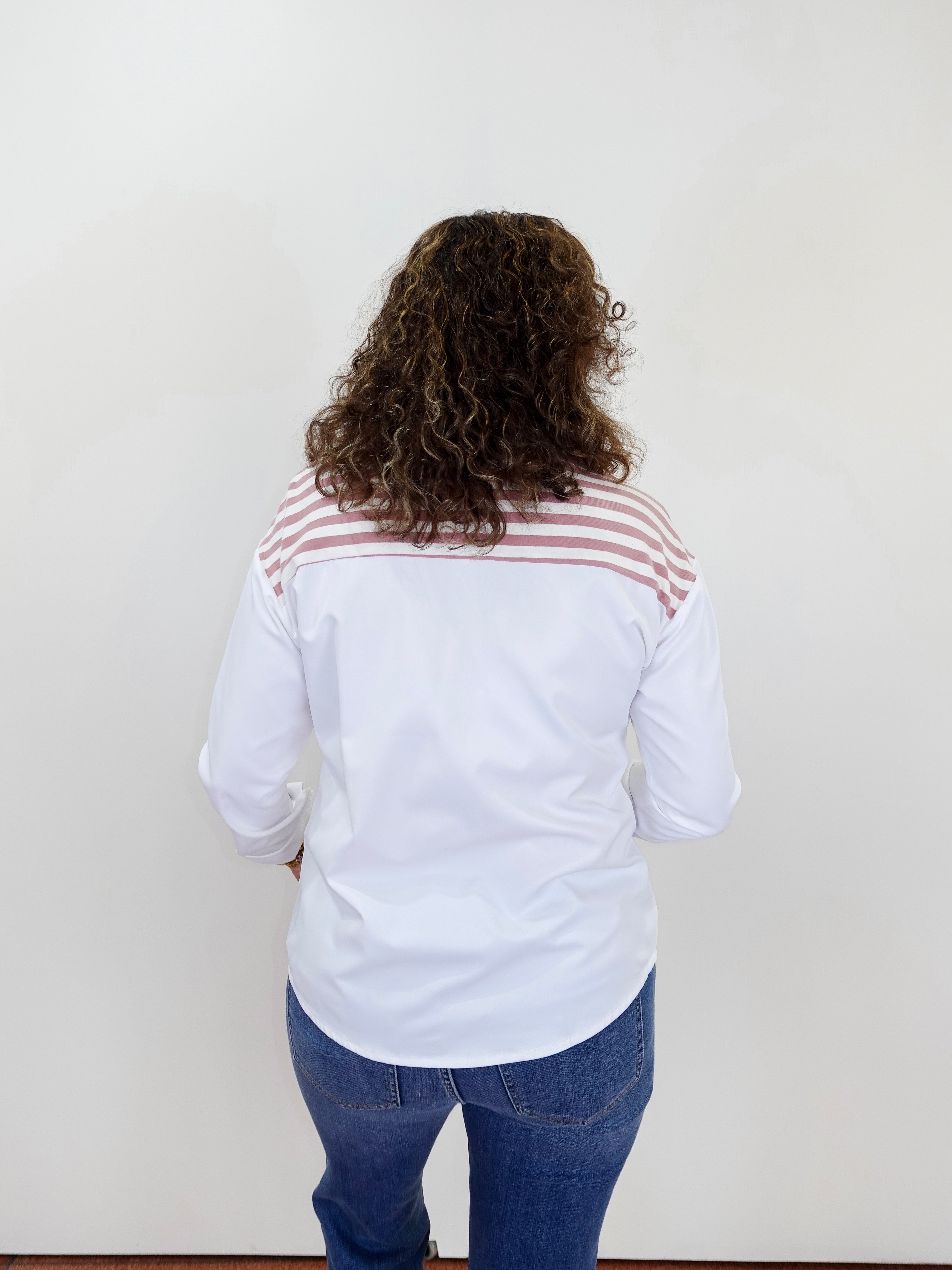 Person wearing a white shirt with a red and black striped pattern on the back, standing against a plain white wall.