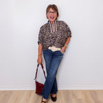 Woman in a leopard print blouse and blue jeans standing against a white wall.