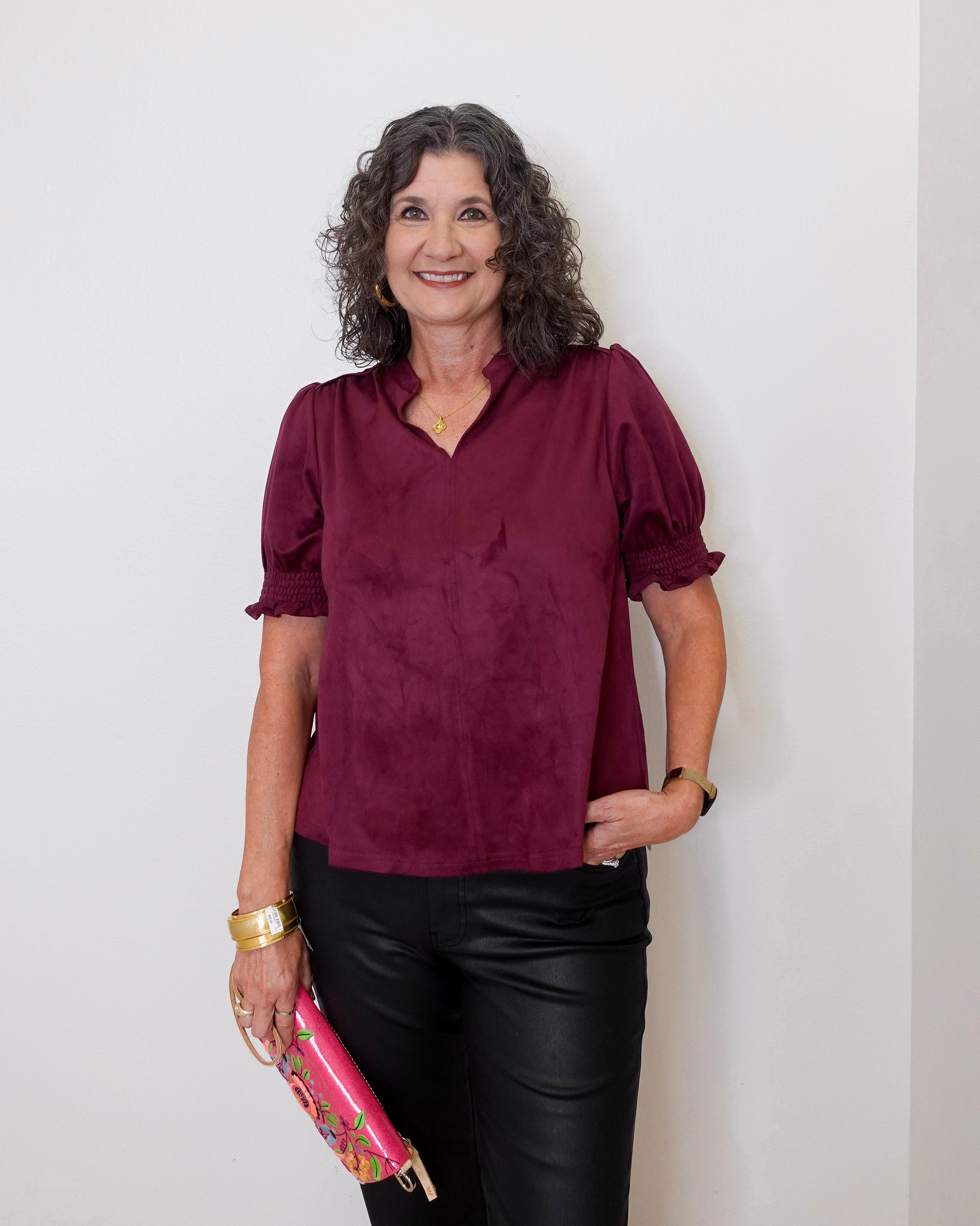 Woman wearing a burgundy blouse and black pants, holding a pink clutch against a white background
