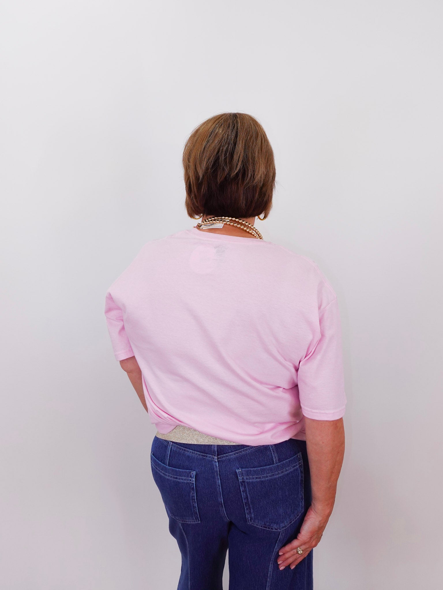 Person wearing a pink shirt and blue jeans from behind on a white background