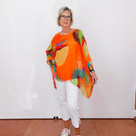 Person wearing a colorful poncho with abstract patterns against a white wall.