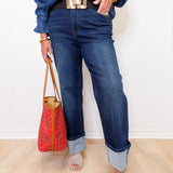 Person wearing blue jeans and a denim shirt, holding a red handbag against a white background