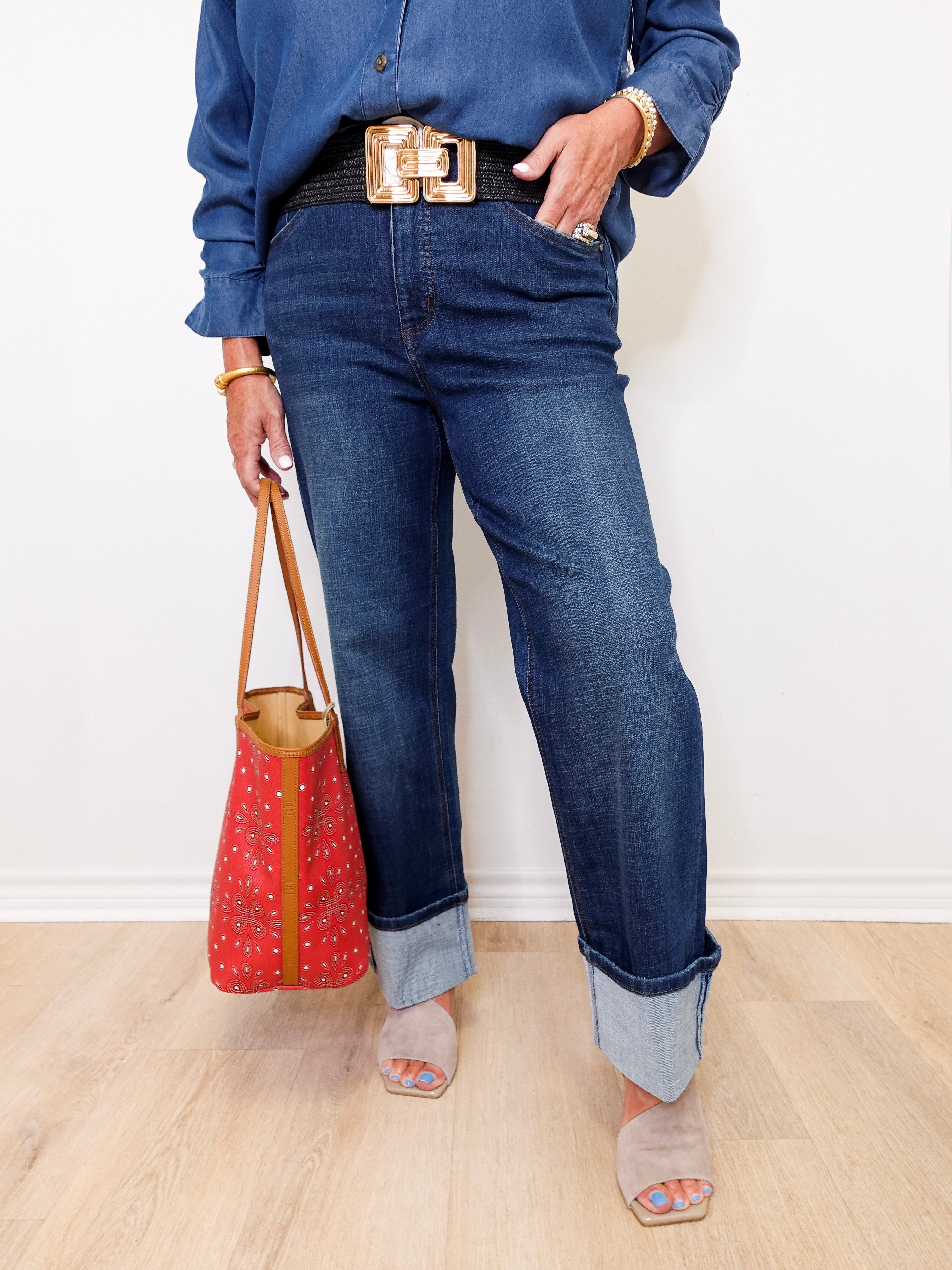 Person wearing blue jeans and a denim shirt, holding a red handbag against a white background